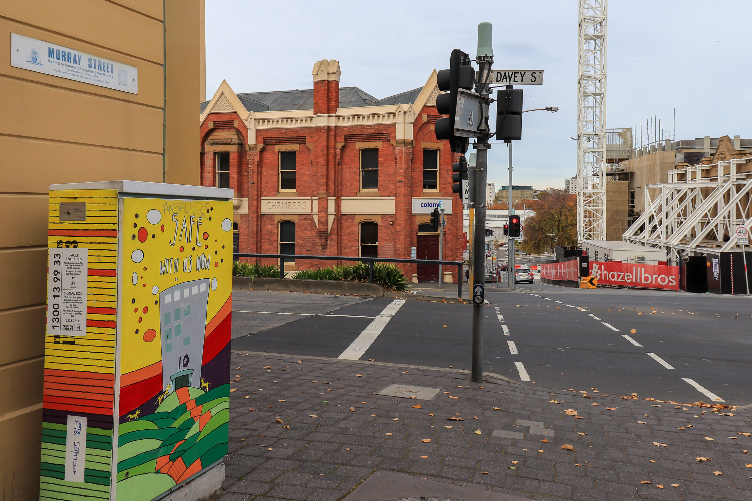 A colourfully pained traffic signal box near a set of traffic lights. On the other side of the street is a building being demolished