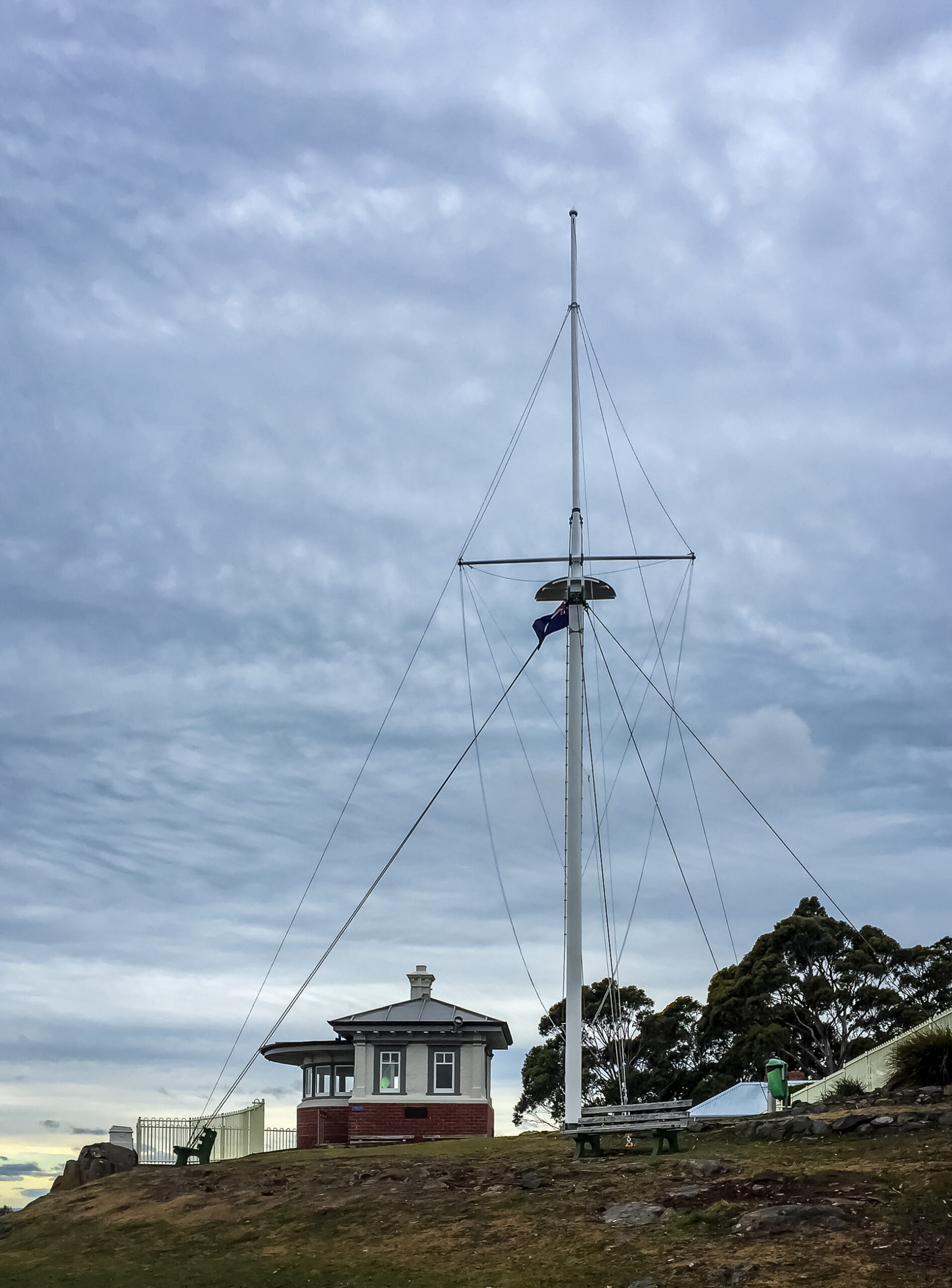A mall brick hut beside a large pole that is held in place by a lot of ropes