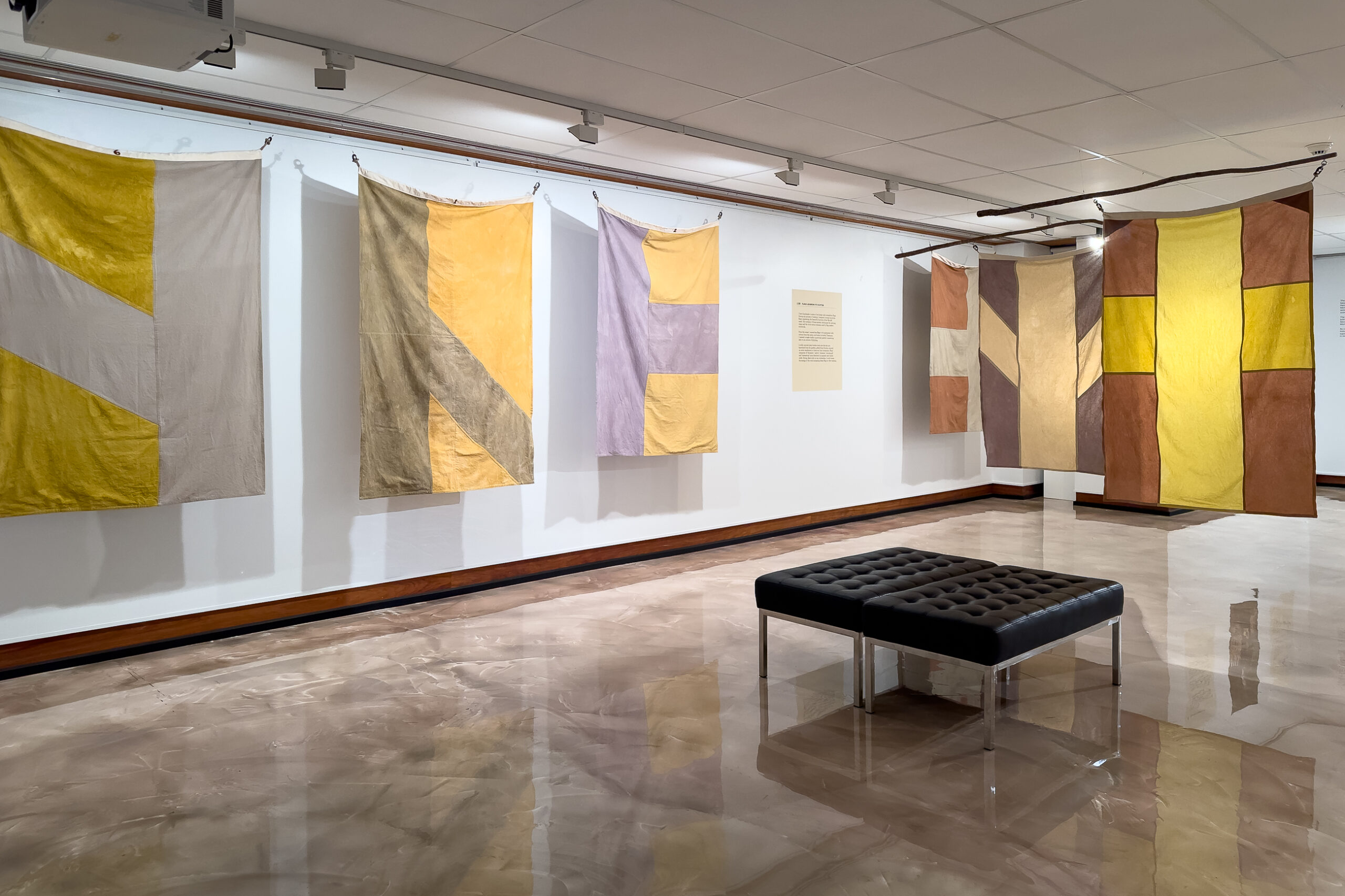 Coloured flags in shades of yellow, brown and grey hang in a gallery