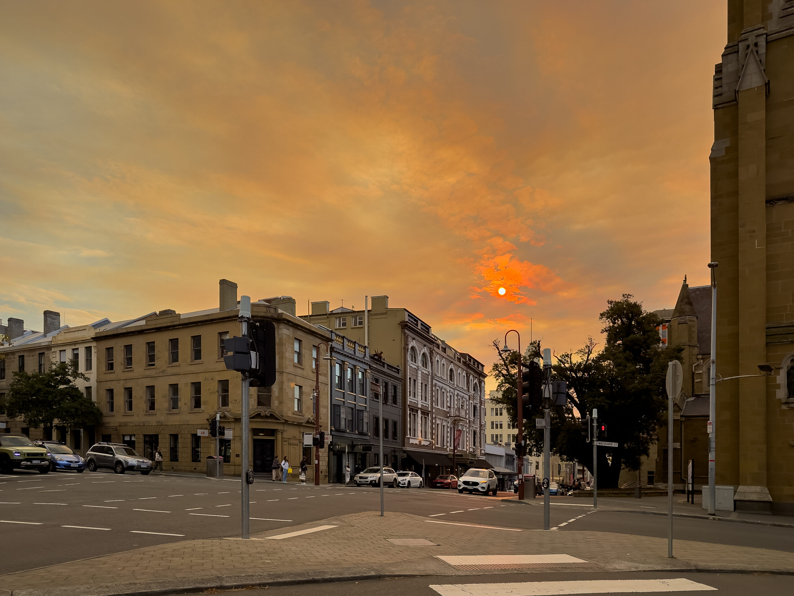 A street corner late in the afternoon. The sky is filled with smoke and the sun is a bright red orb