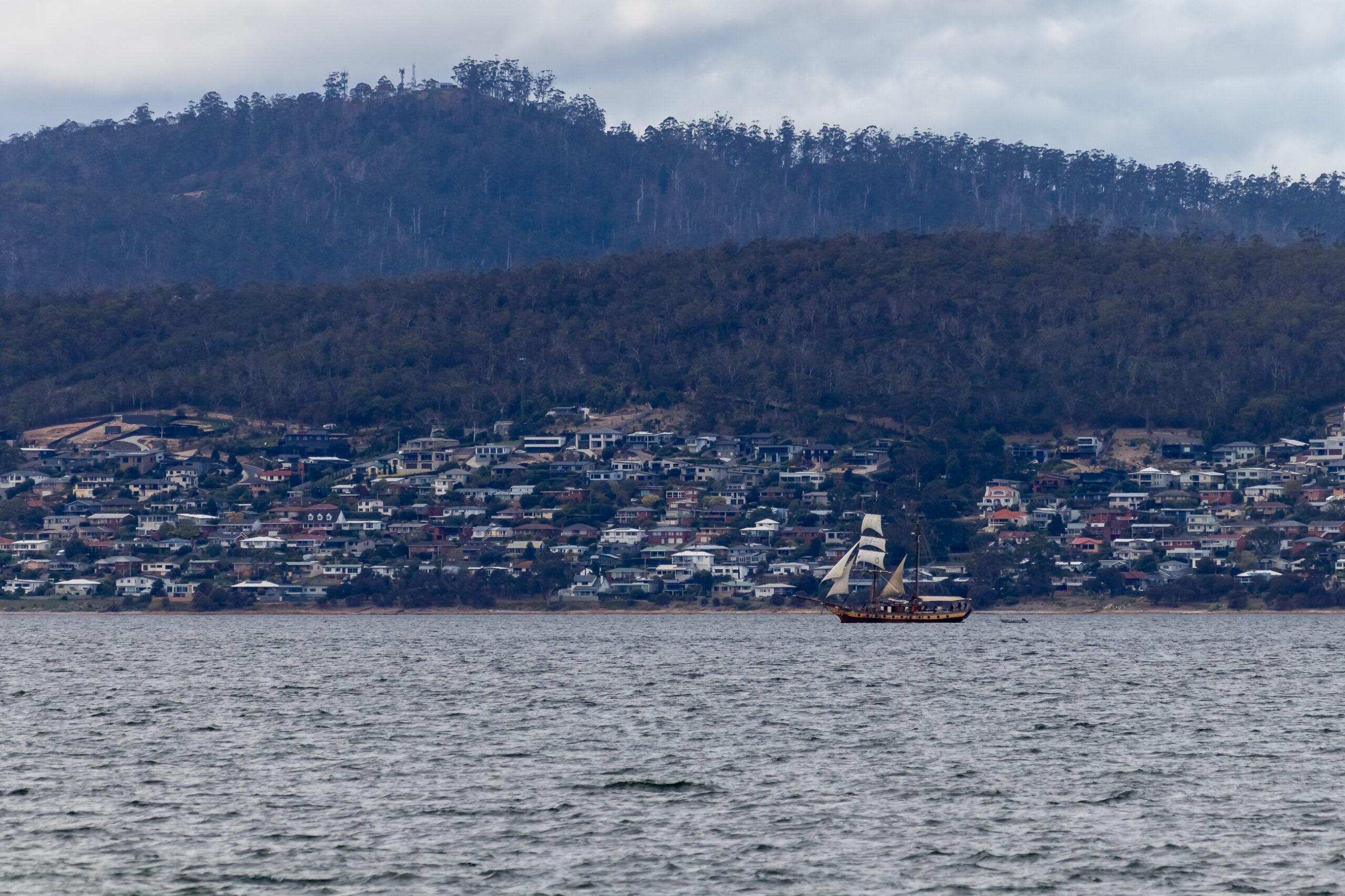 A tall ship sailing boat is in the distance on the river