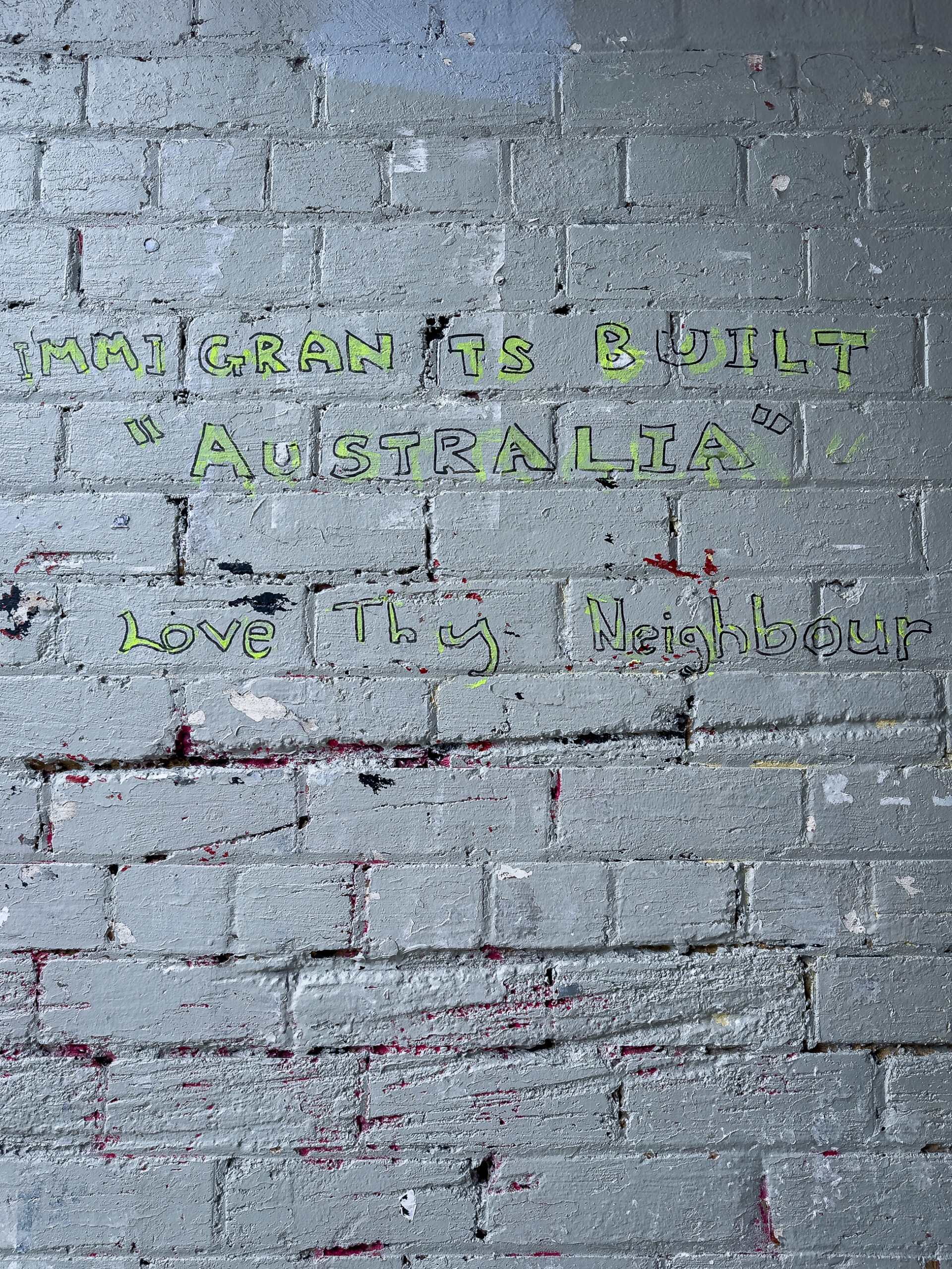 Text painted on a white painted wall "Immigrants built 'Australia' Love they neighbour"