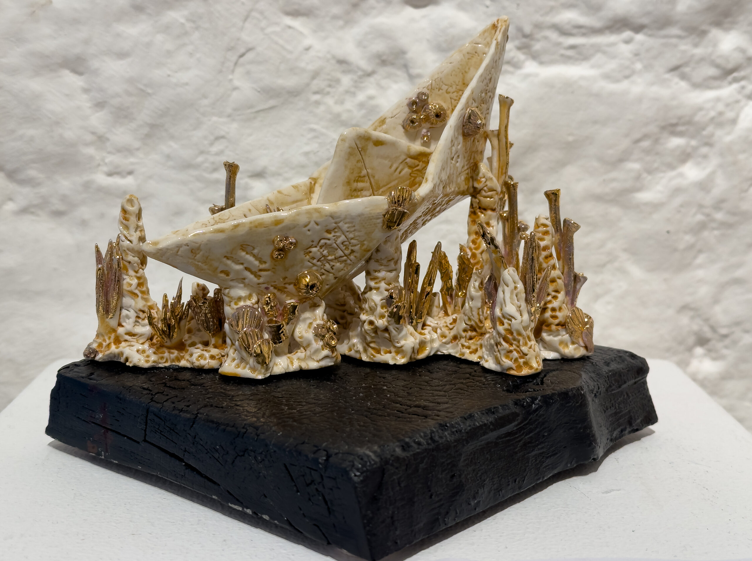 A golden sculpture of large sails on a wooden stand