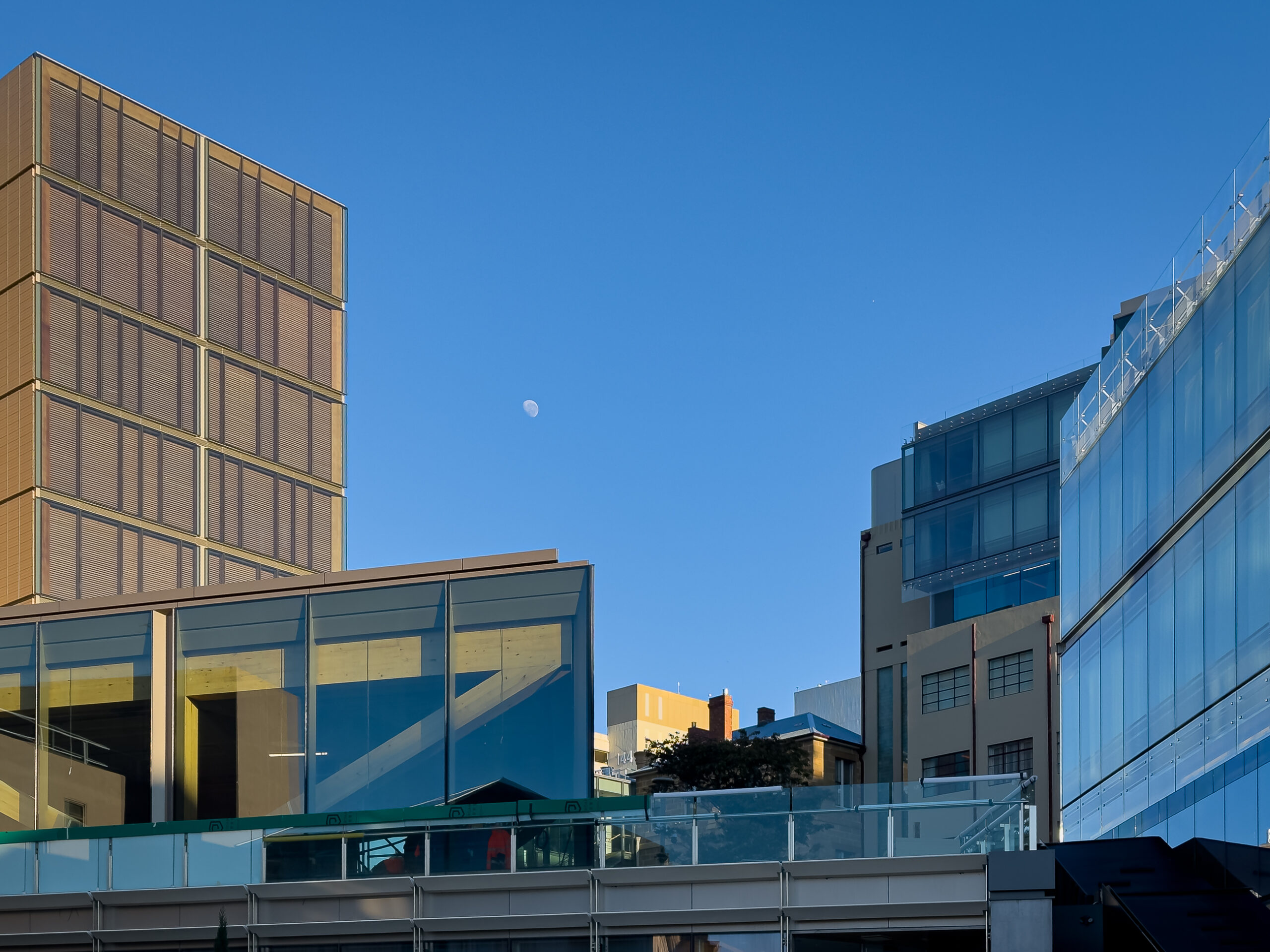 The full moon, very small, in the blue sky between two glass buildings