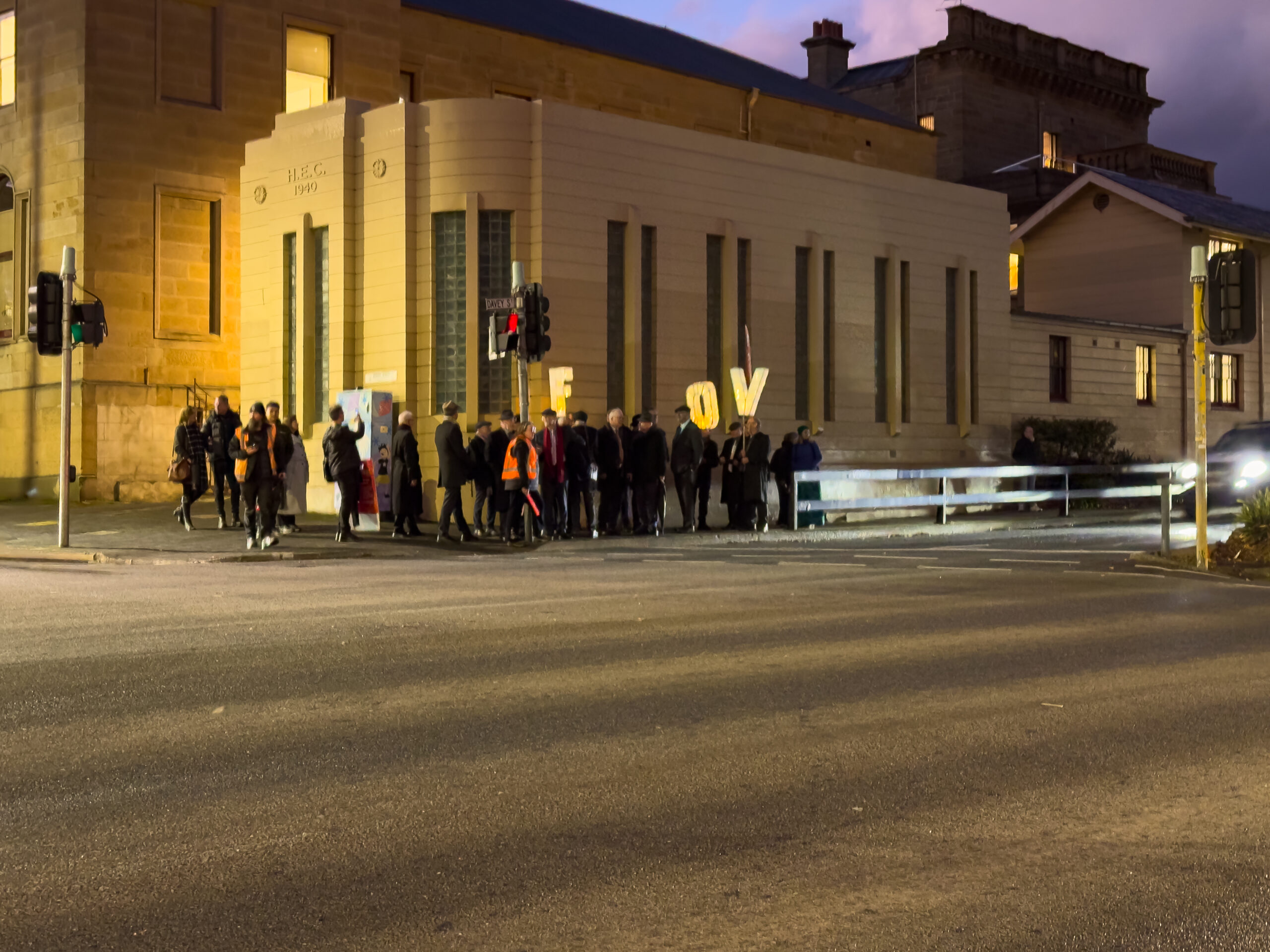 A group of people standing on a street corner in the street lights holding lights with the letters F O and V.