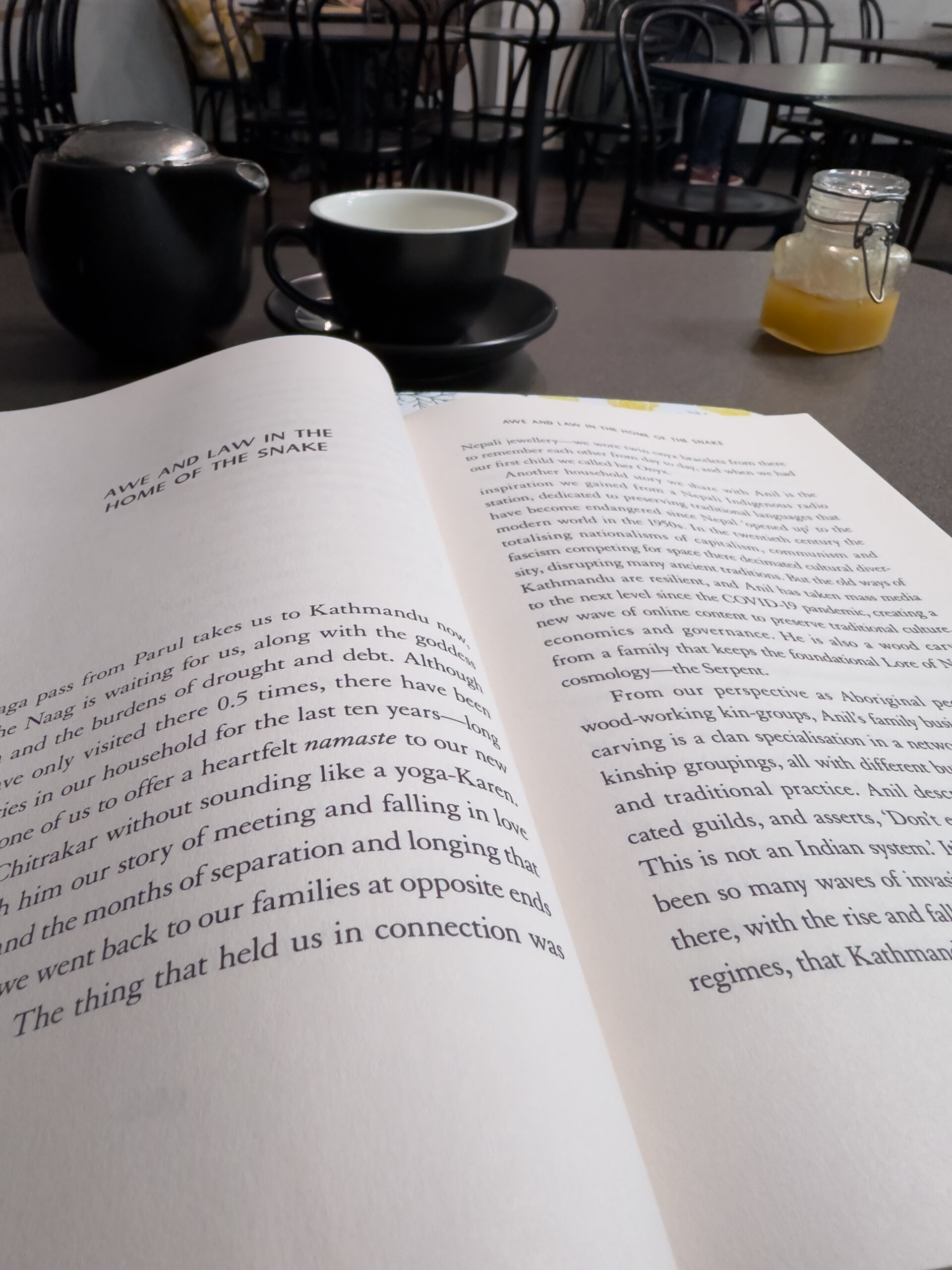 An open book on a table. There is a teapot and a cup behind it