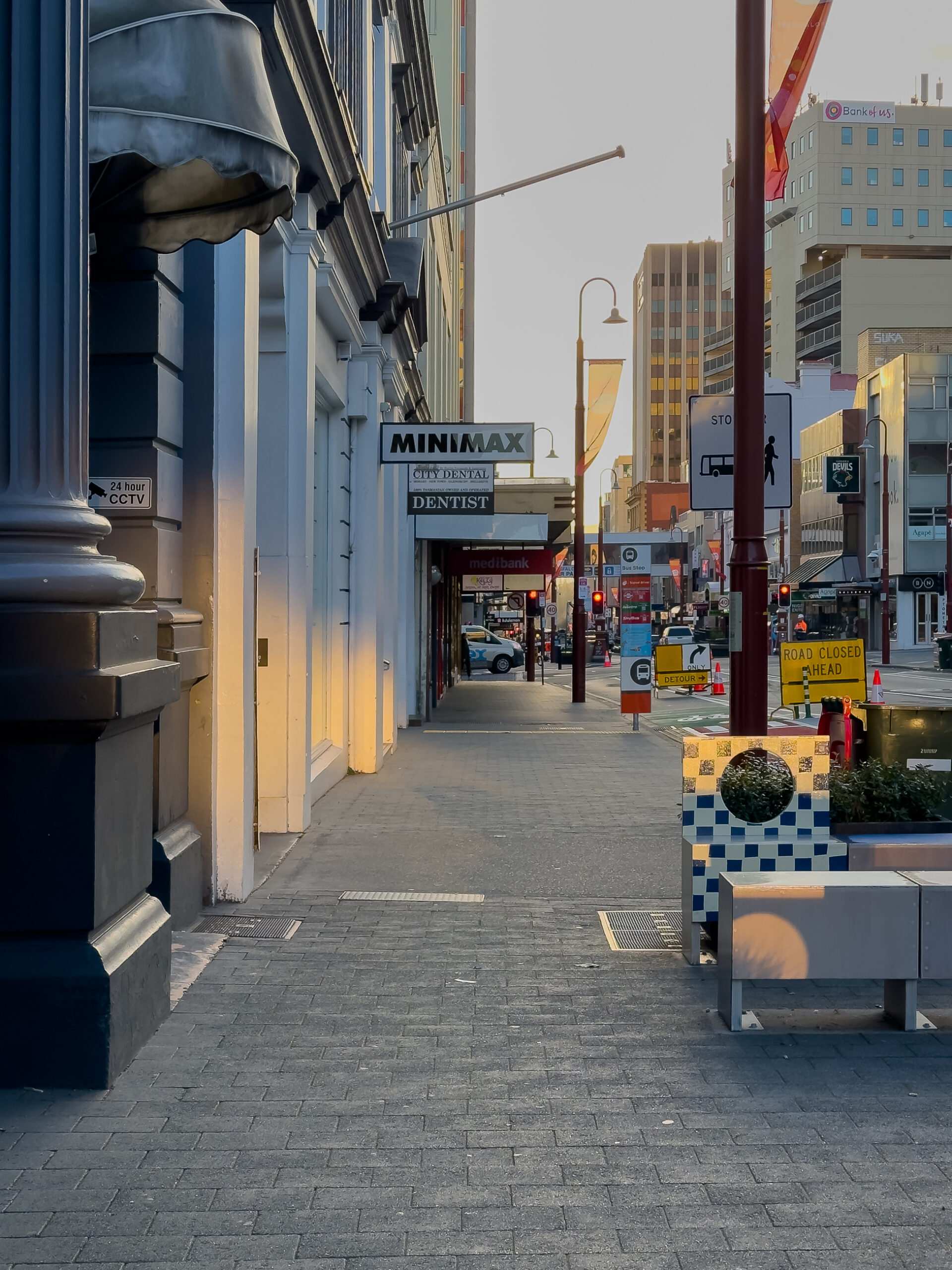 A street view. There is light reflecting onto the facades of the buildings and onto the ground