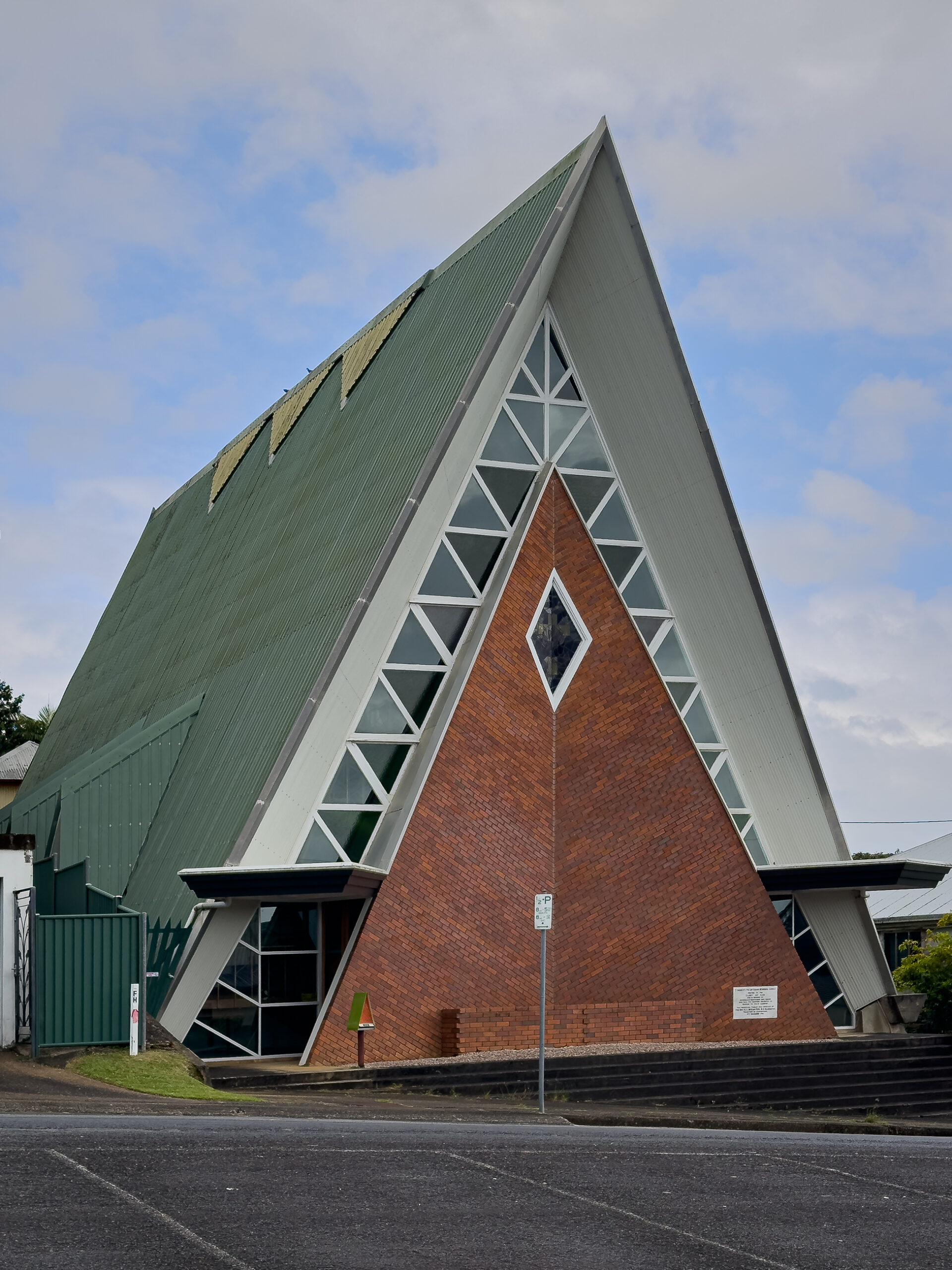 A modernist church that is triangle shaped. It is made from brick and has a green roof