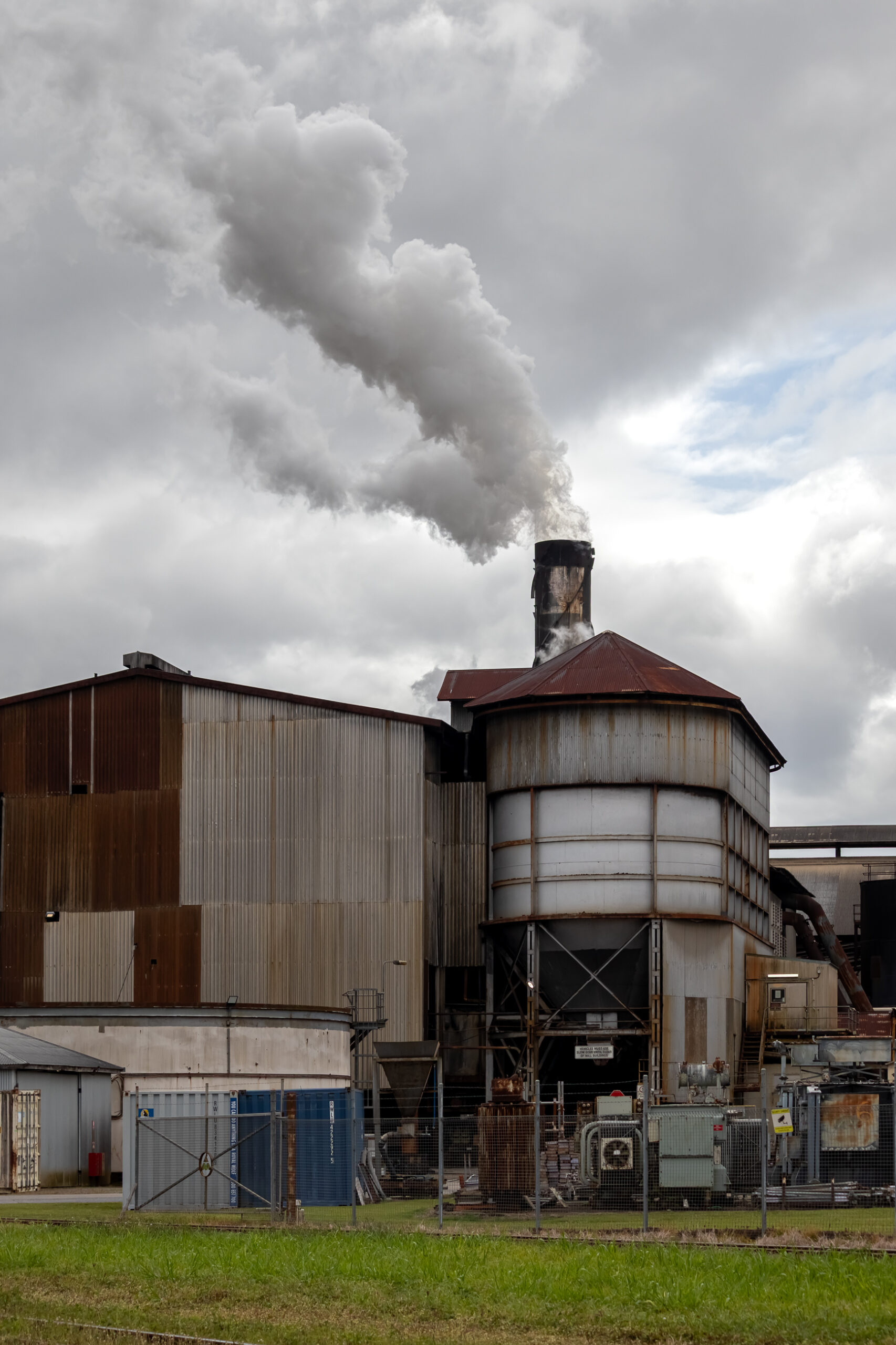 A brown factory with a smoke stack sending smoke into the air