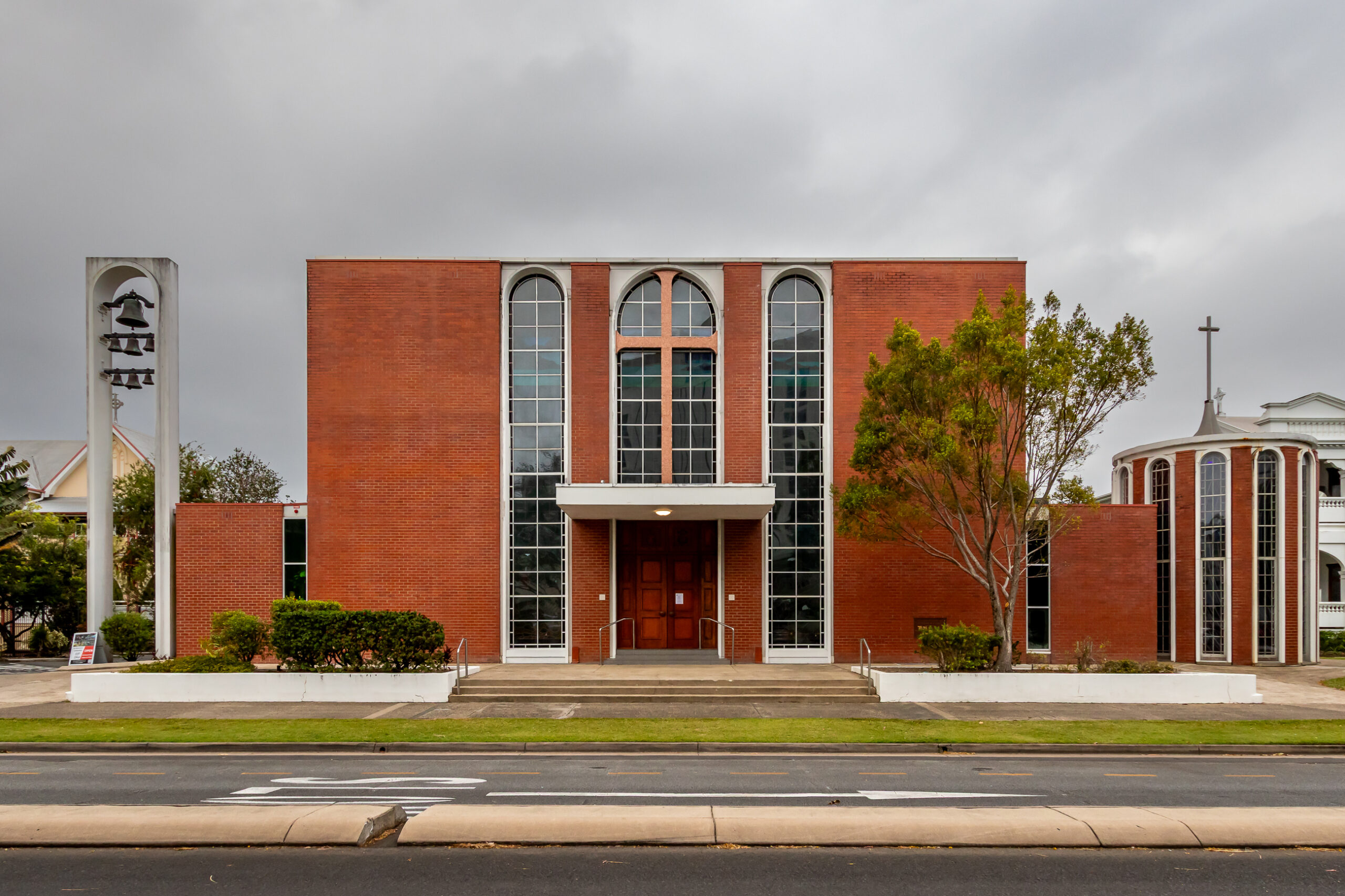 a red brick modernist church with striking arch windows and a set of bells to the side