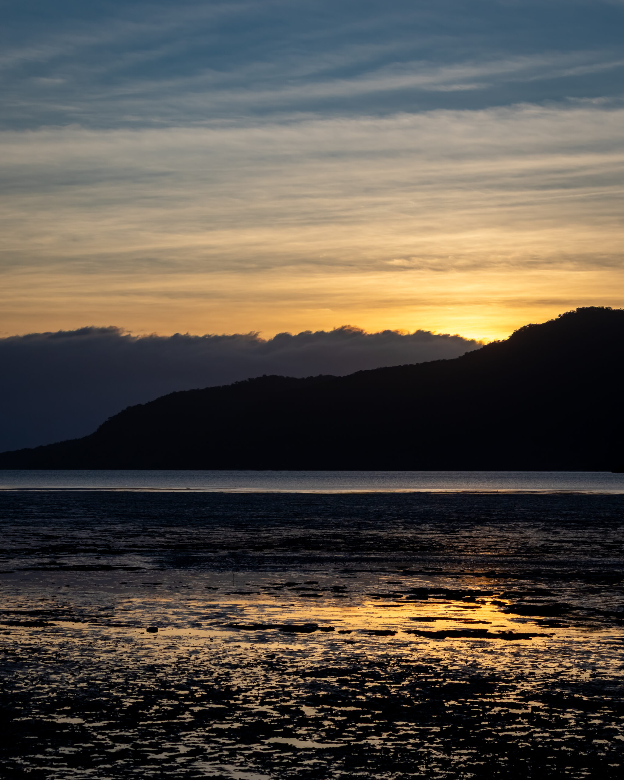 A sunrise over the water with hills in the background