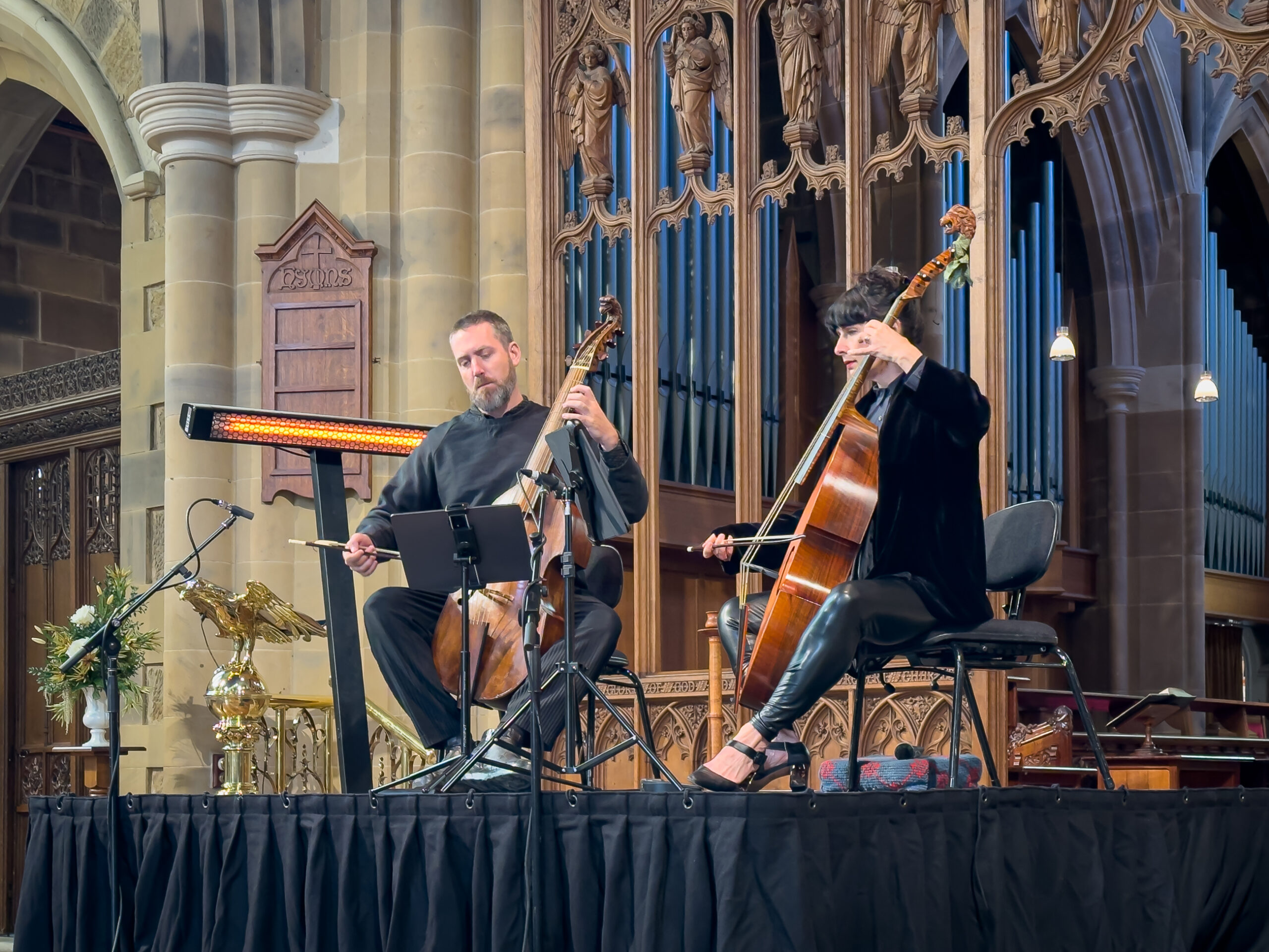 Two musicians with viol da gamba on a stage in a sandstone cathedral