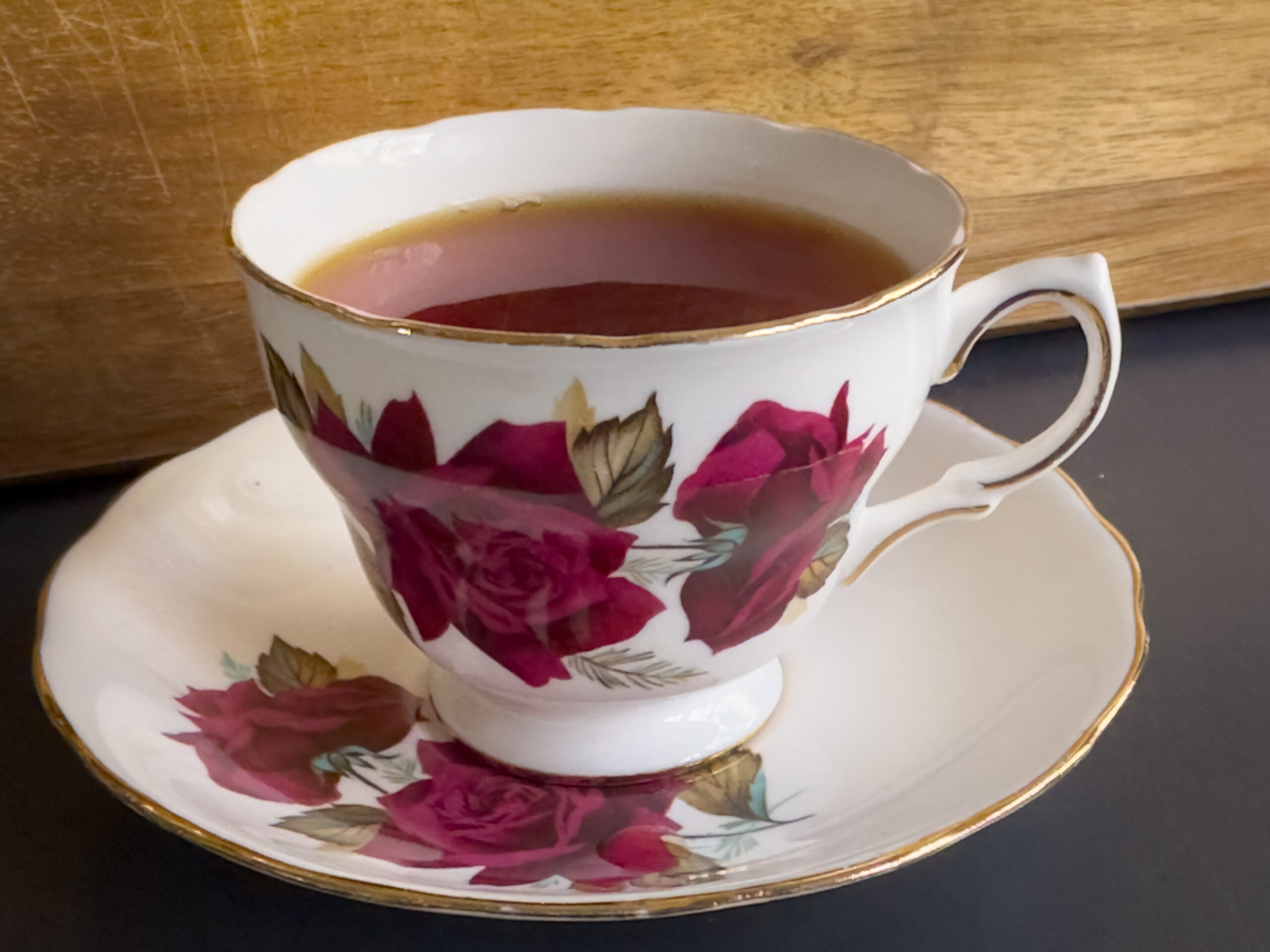 an old fashioned tea cup with red roses on the side of the cup. The cup and saucer are gold-trimmed